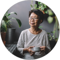 Older woman wearing glasses holding a mug while standing next to indoor plants
